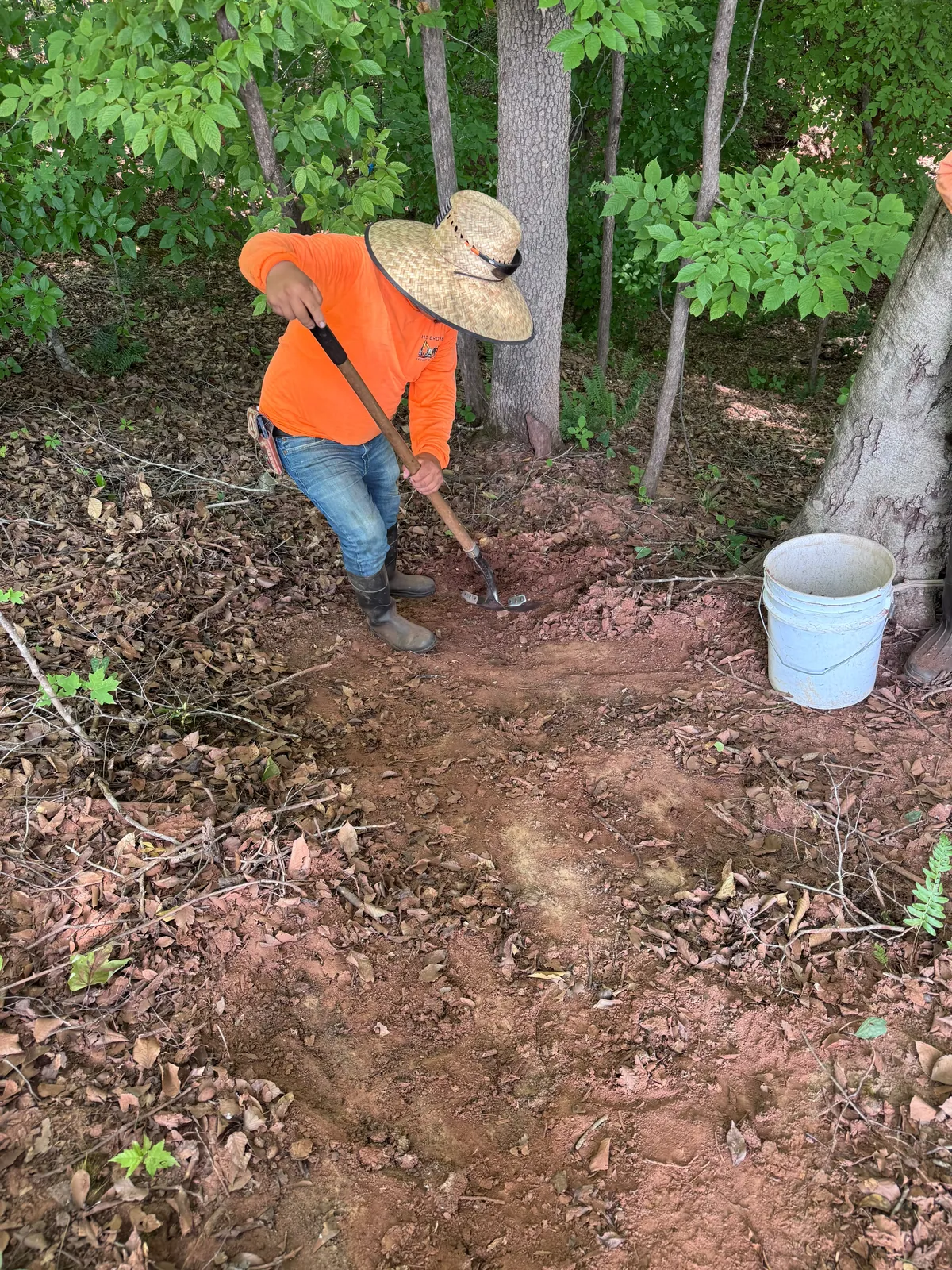 Crew member removing sediment by hand in a wooded swale